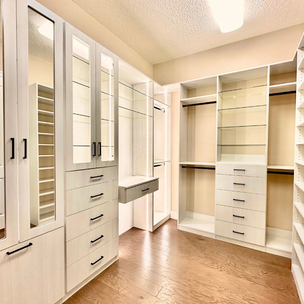 Modern walk-in closet with white cabinets, drawers, and mirrors.