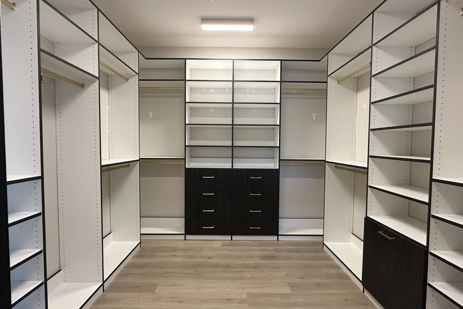 Modern walk-in closet with white shelves and black drawers.