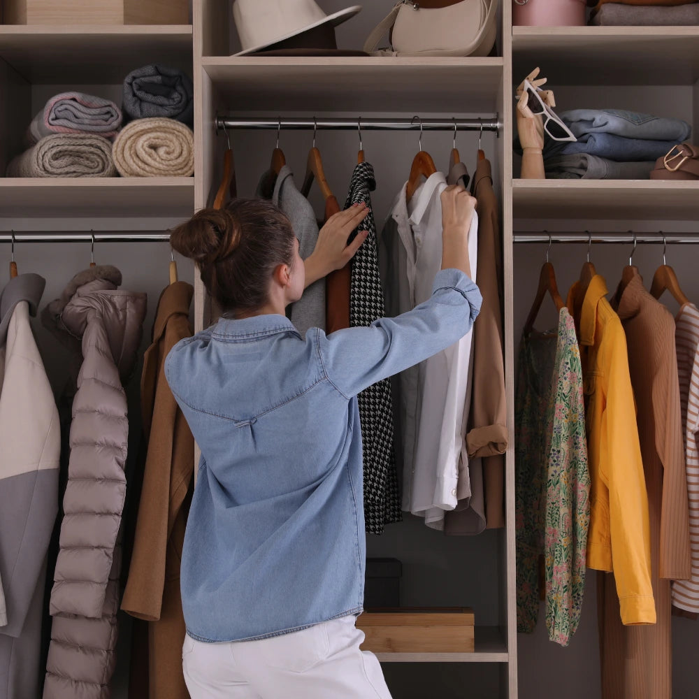 Person organizing clothes in a wardrobe with shelves filled with folded garments.