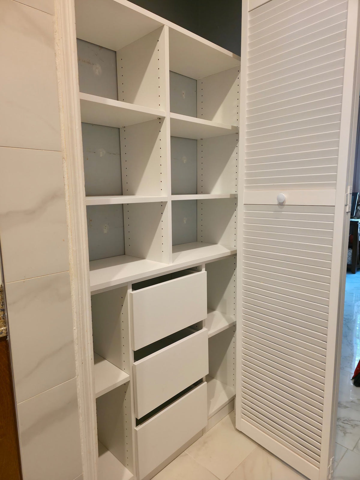 Closet with shelving, drawers and a louvered door on a marble floor