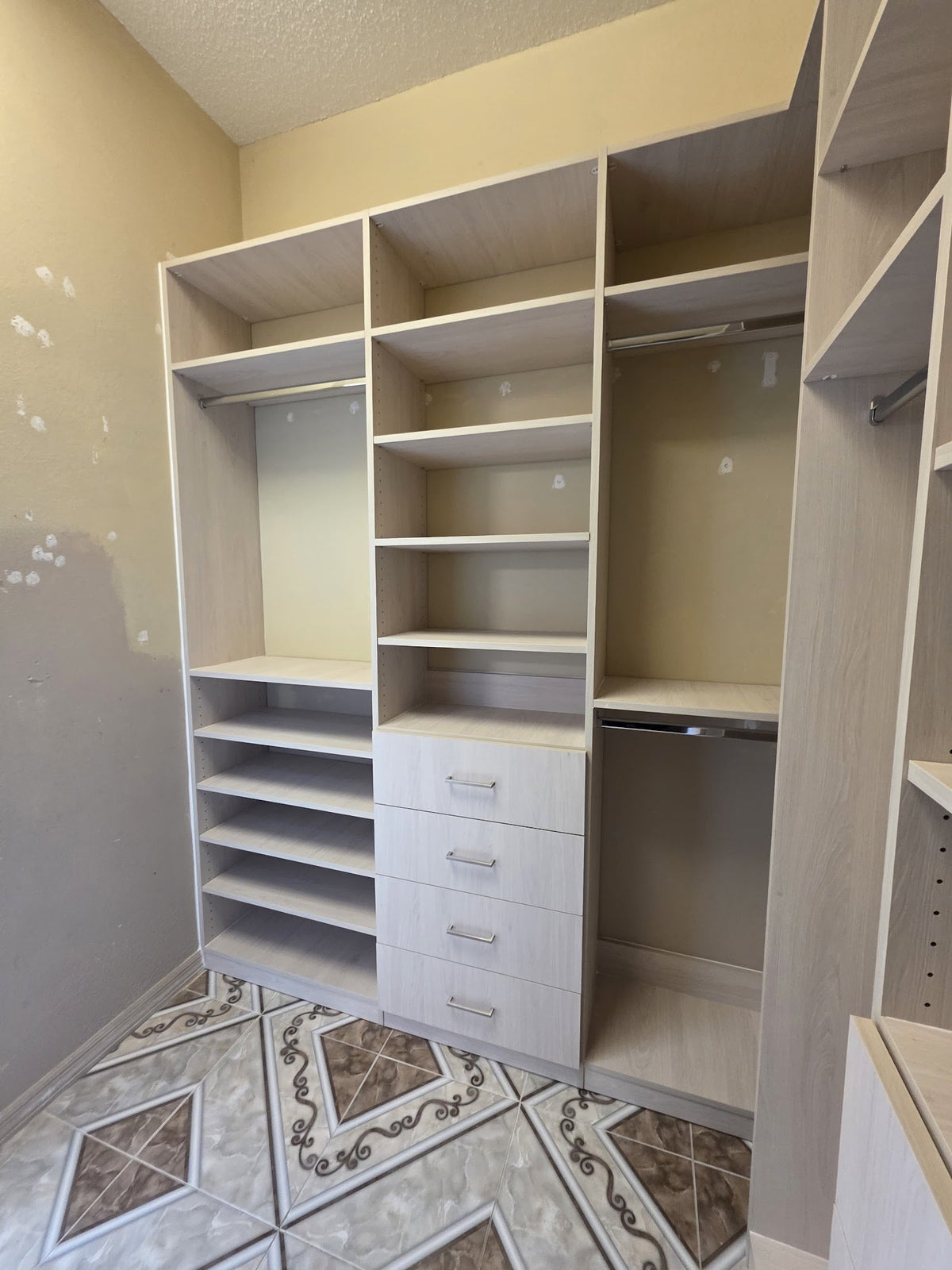 Walk-in closet with light wood-grain shelving and drawers on a patterned tile floor