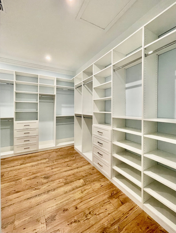 Long white walk-in closet with shelving on both sides and drawers