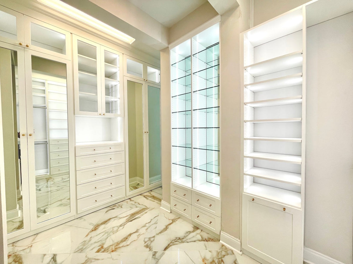 Walk-in closet with glass-front cabinets and lit shelving over a marble floor