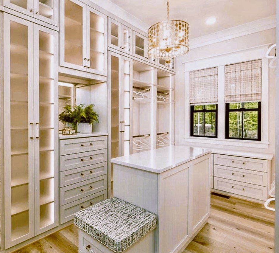 Walk-in closet with glass-front cabinets, a center island, a bench and a chandelier