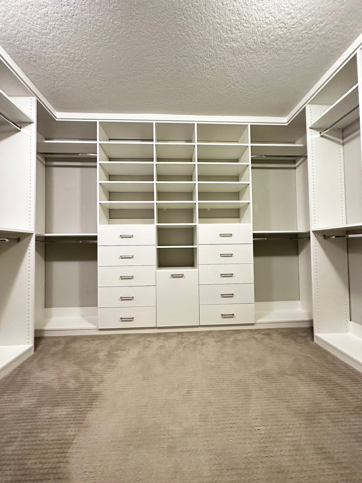 Carpeted walk-in closet with a central wall of drawers and shelves