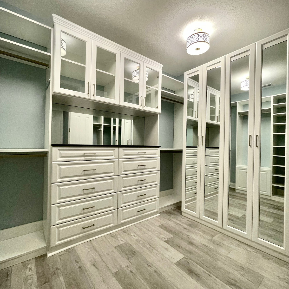 Walk-in closet with glass-front and mirrored cabinets over a drawer bank
